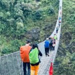 Un puente colgante que comunica dos montañas del Himalaya cruzándolo un grupo de aventureros
