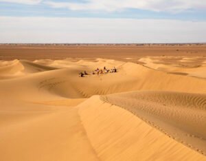 Imagen en la que se ve las dunas del desierto y un grupo de gente caminando por ellas